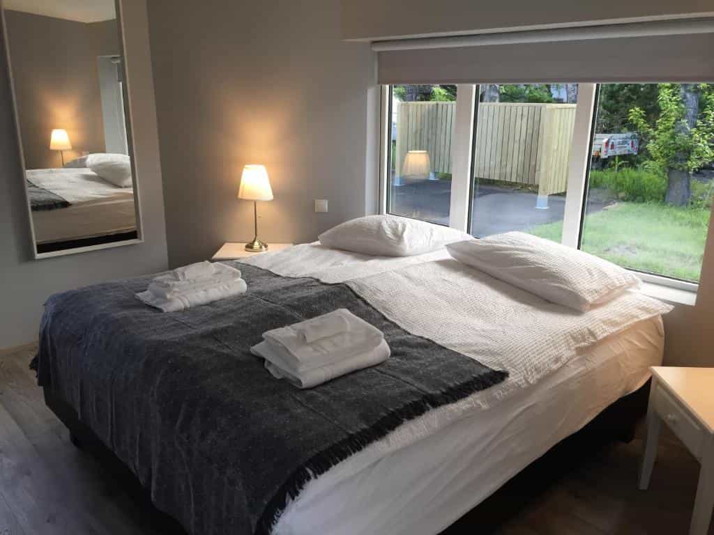 Bedroom with large bed, white linens, dark throw, and bedside lamp near window at Reykjadalur Guesthouse.