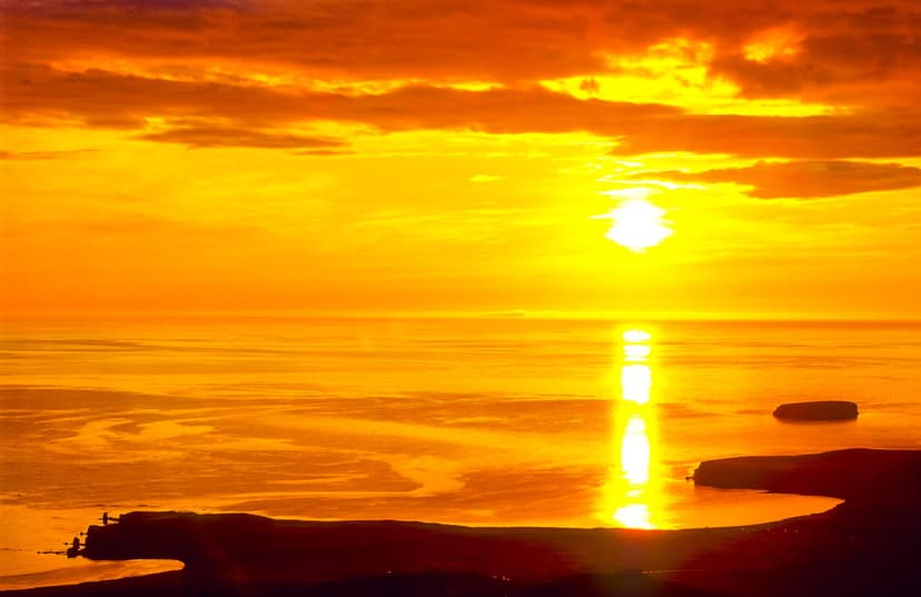 Bright golden sunset over the ocean with silhouetted coastline.