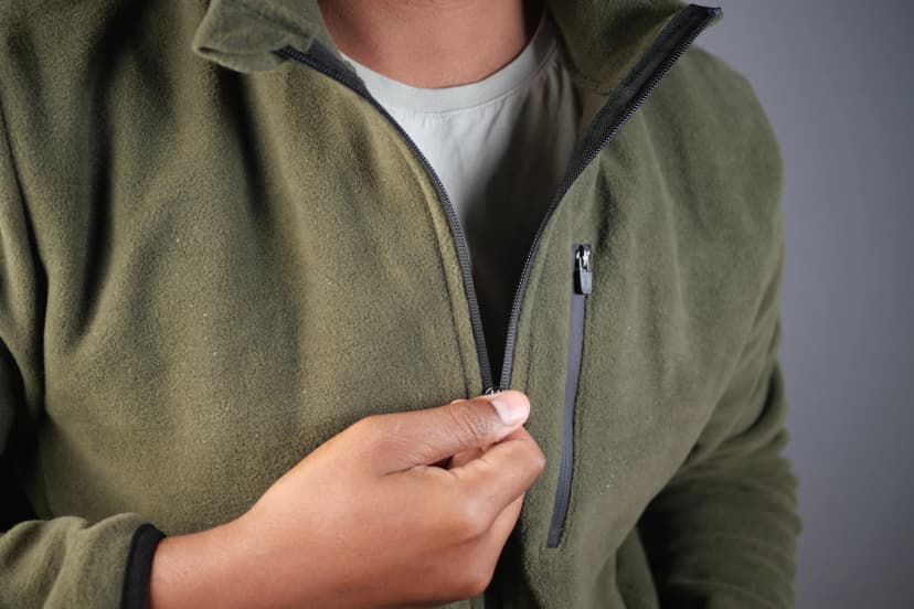 Person adjusting green fleece jacket in indoor setting