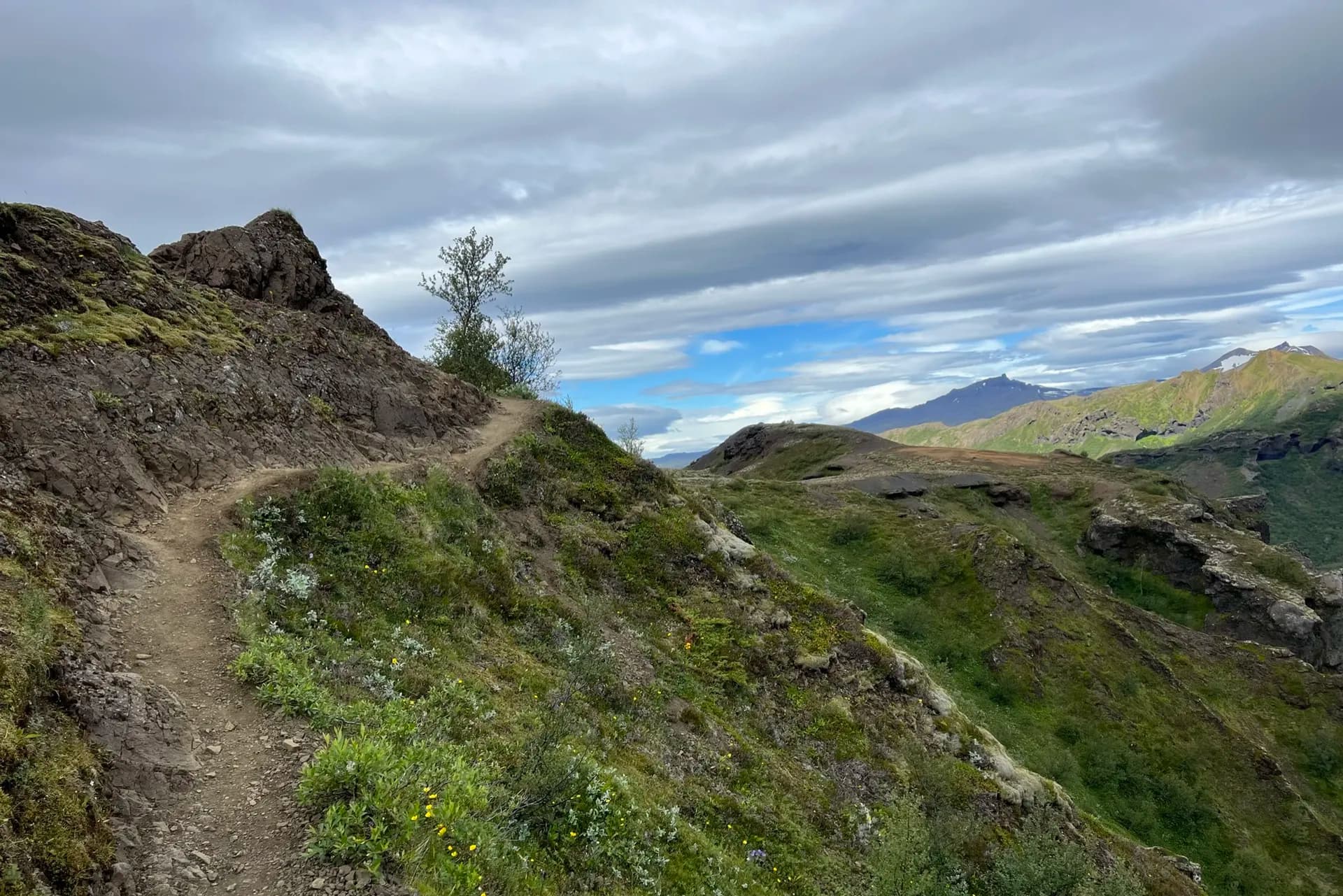 Hiking trail on Fimmvörðuháls mountain pass in Iceland with rocky terrain and green hills under a cloudy sky.