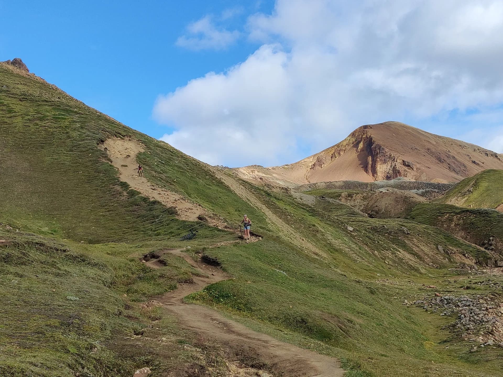 Hikers on a dirt trail winding through green, mountainous terrain on the Laugavegur trail in Iceland.