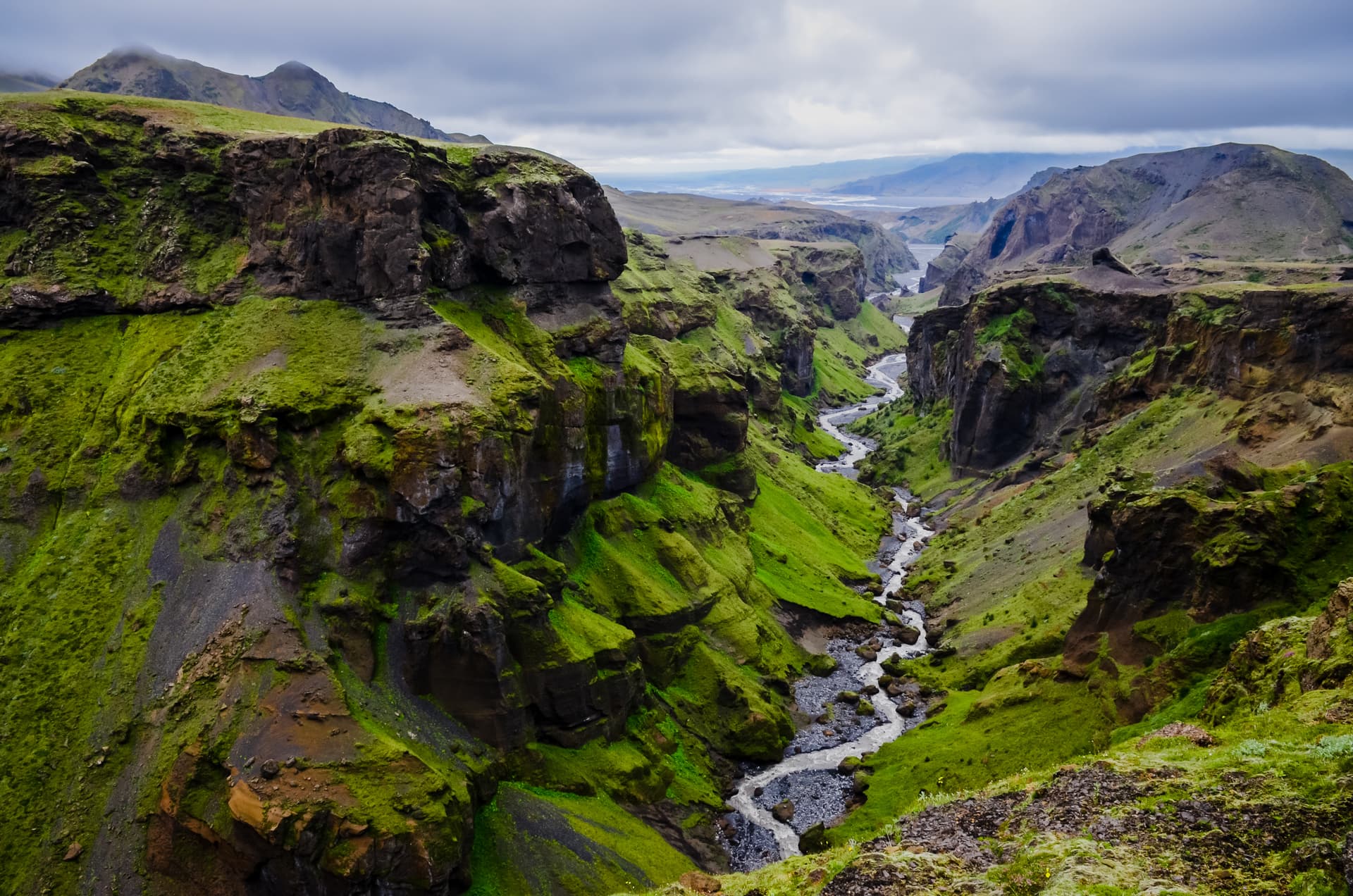 River winding through Thorsmork Canyon with steep, moss-covered cliffs under a cloudy sky.