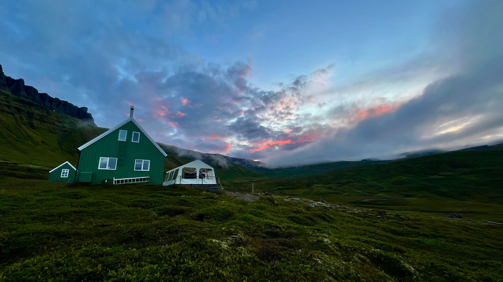 Green hut under a pink and blue sky in a mountainous landscape