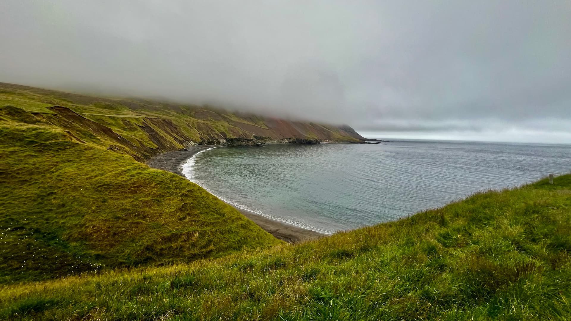 Misty bay below green slopes and rocky coastal cliffs