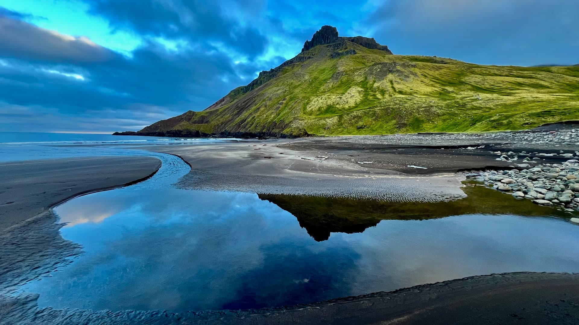 Green mountain peak reflected in water on a black sand beach