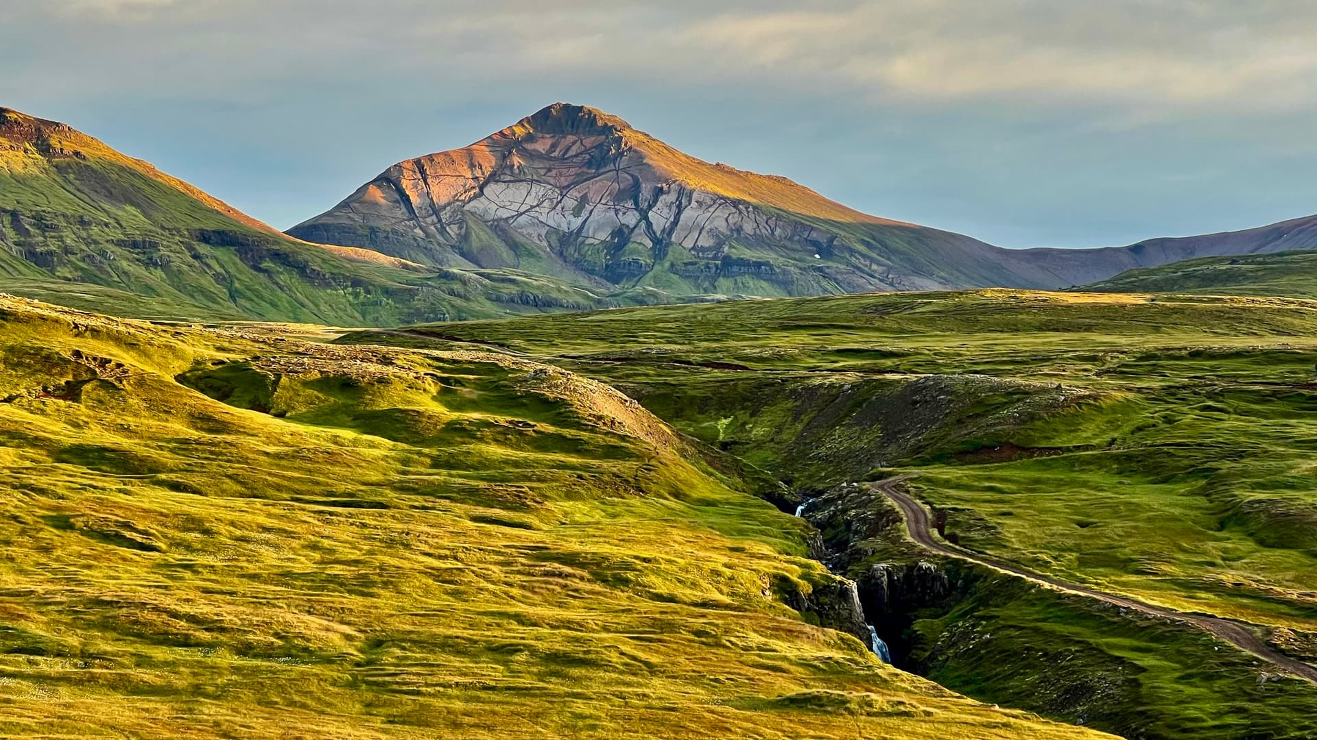 Mountain peak illuminated by warm morning light over green valley landscape