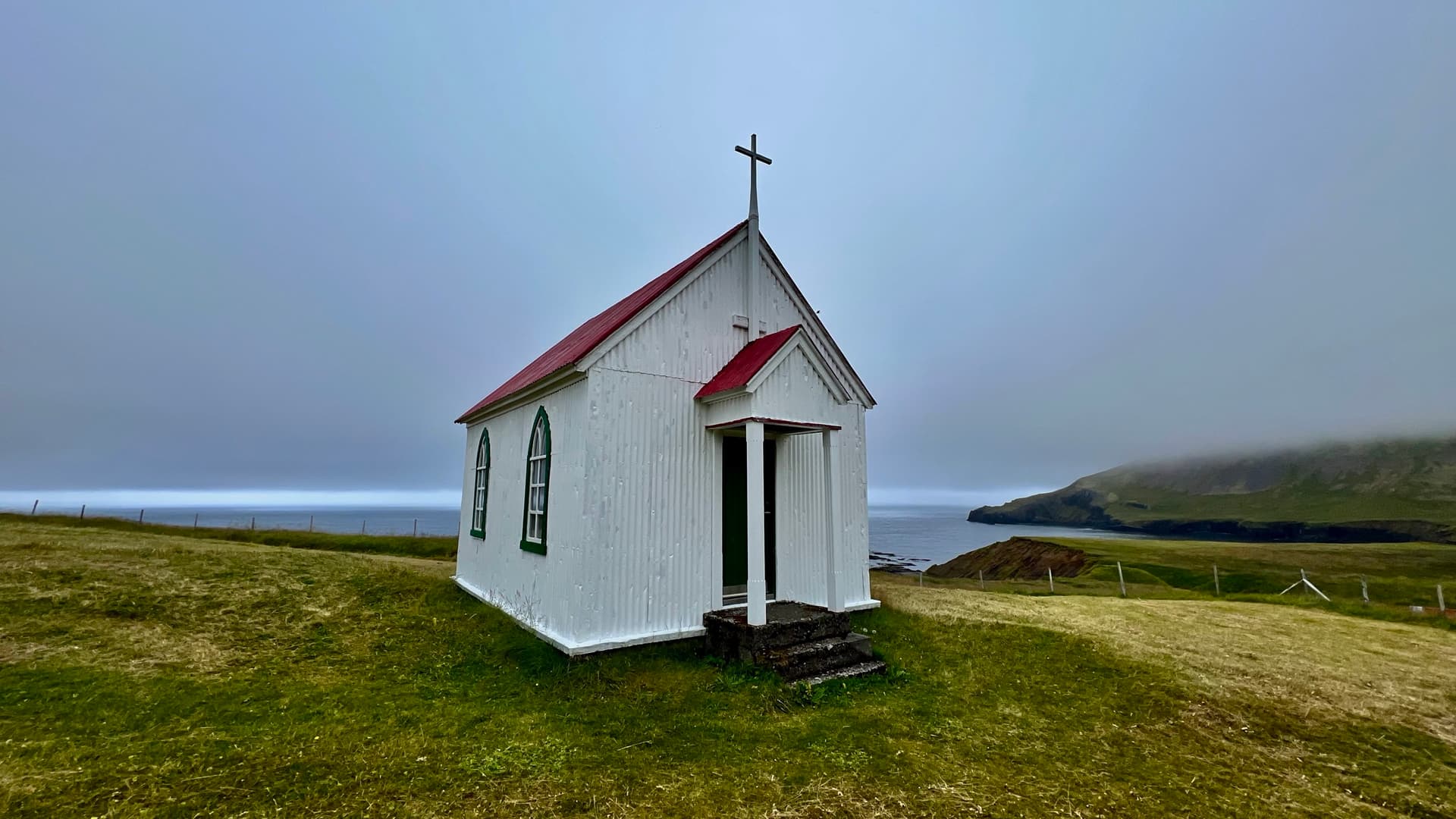 Small white church with red roof in a misty coastal landscape