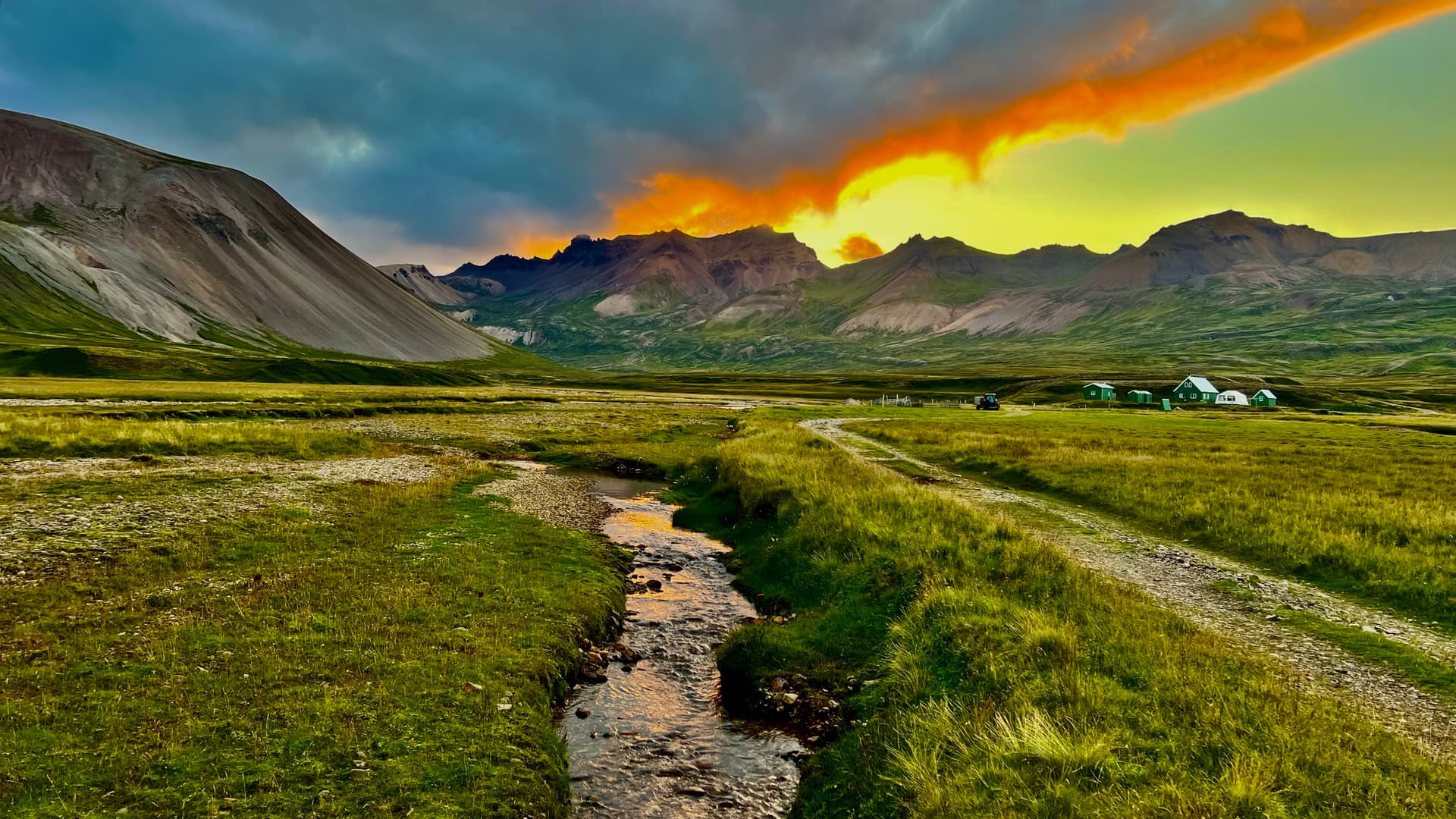 Stream running through a green valley with mountains and vibrant sunset sky