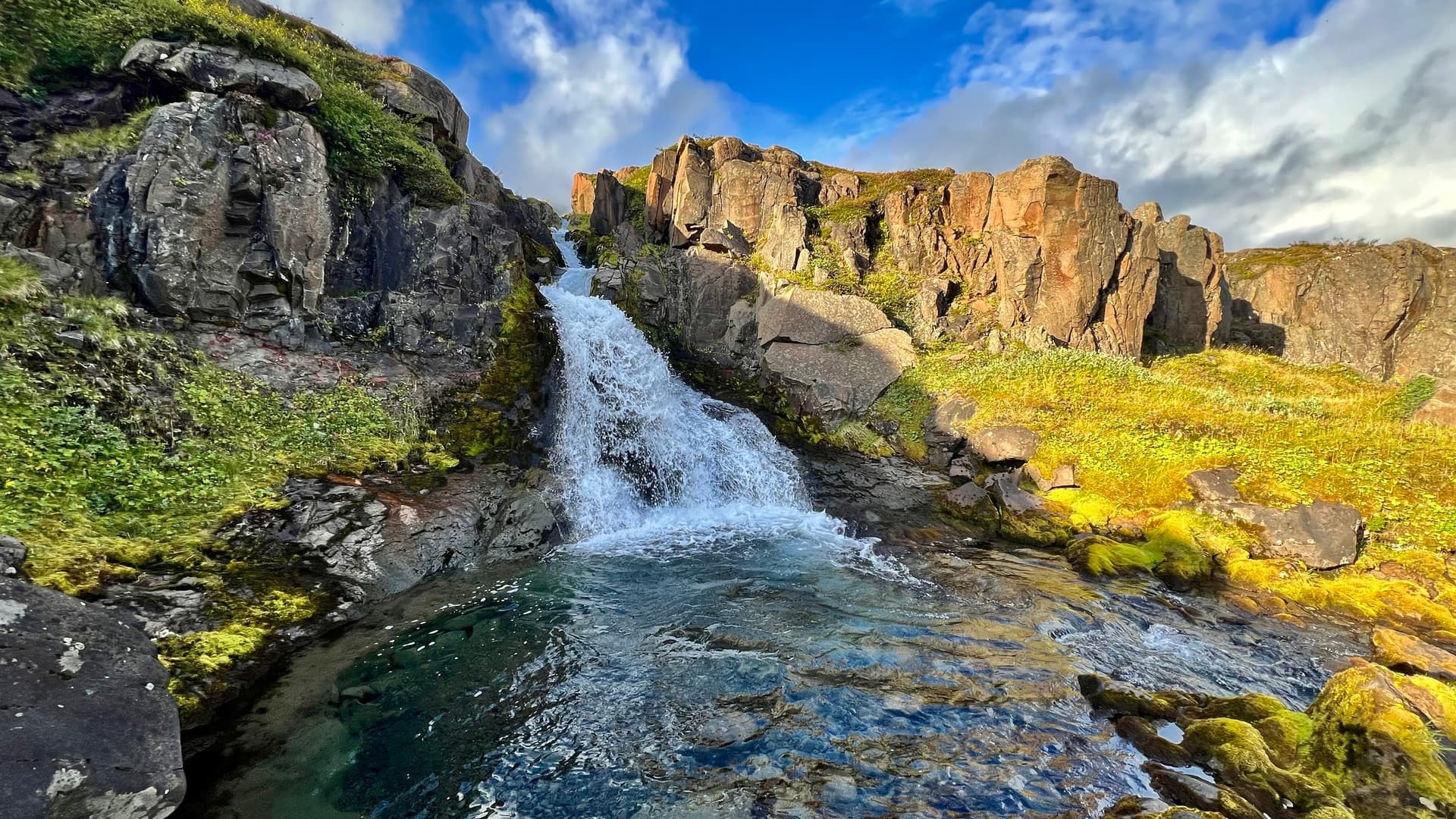 Waterfall cascading into a rocky canyon pool with mossy banks