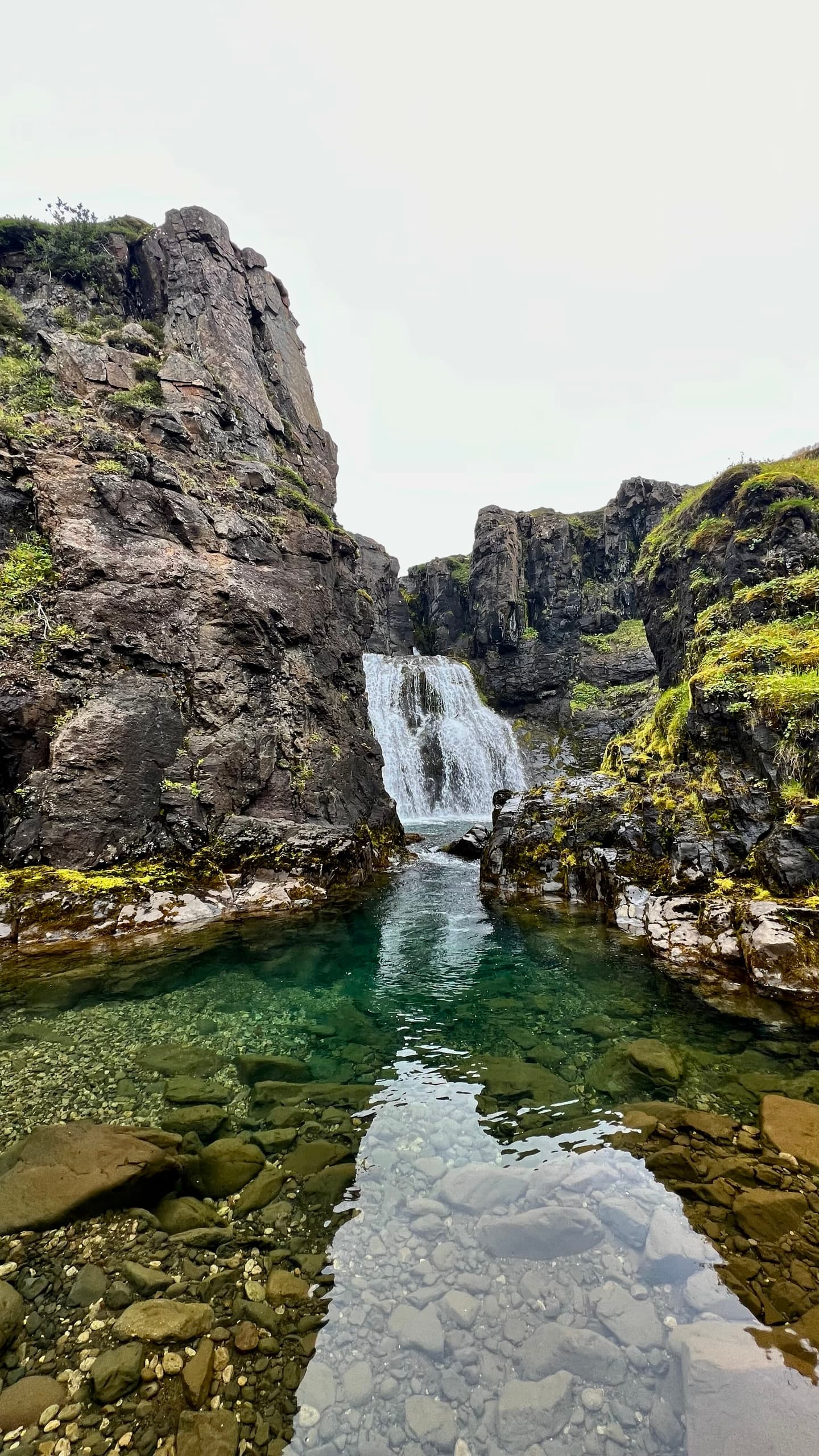 Waterfall in a rocky gorge with clear green pool and mossy stones