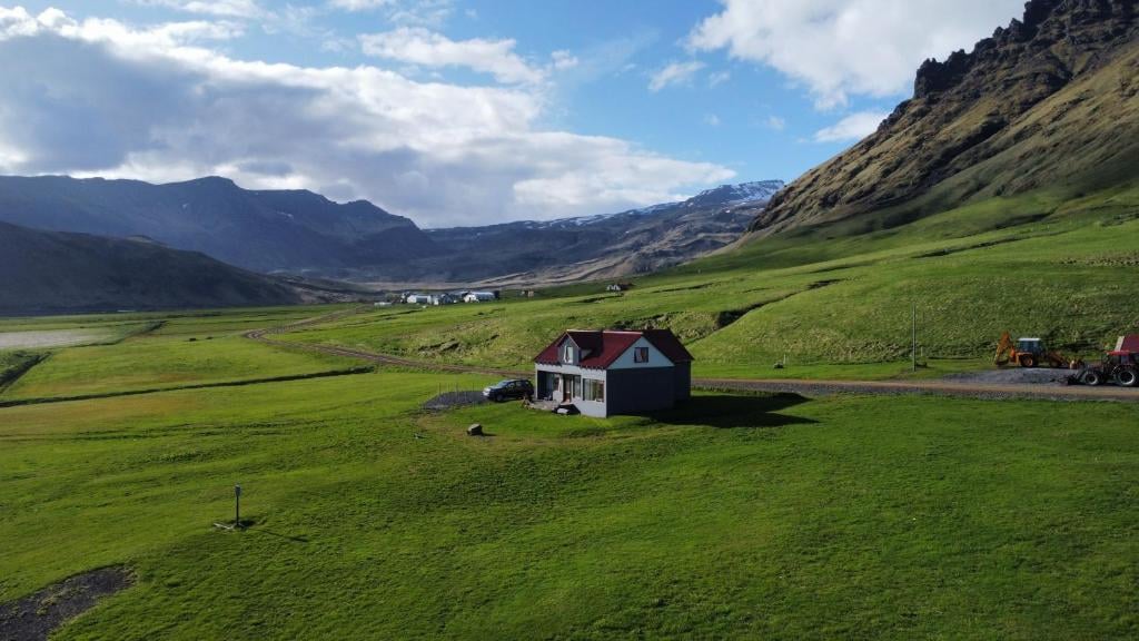 Guesthouse Rauðafell i en grøn dal med bjerge og blå himmel.
