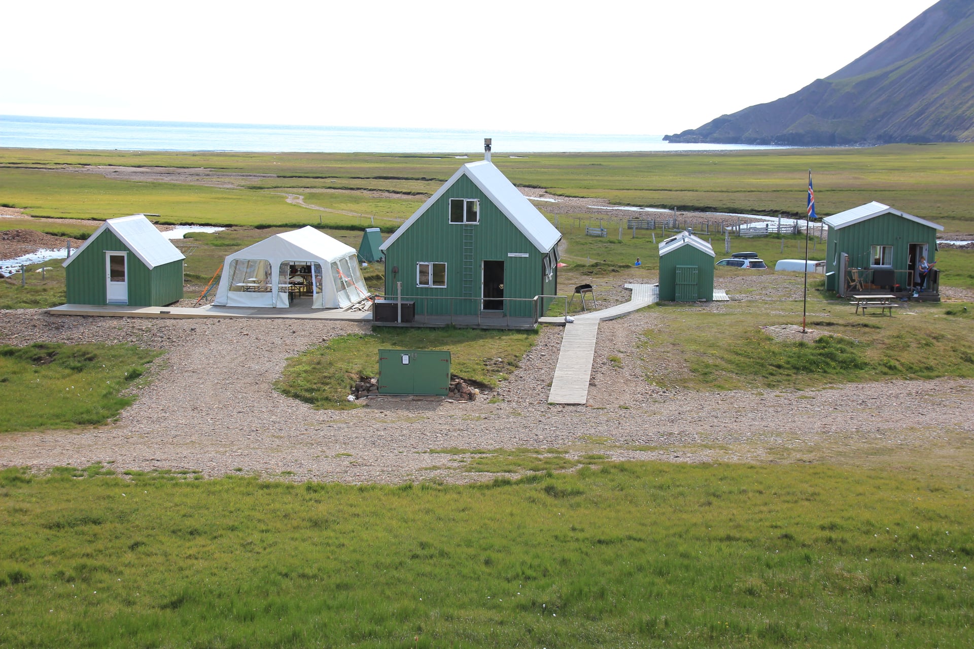 Grønne hytter og et hvidt telt ved Breiðavík ved havet med et stort græsareal og bjerg.