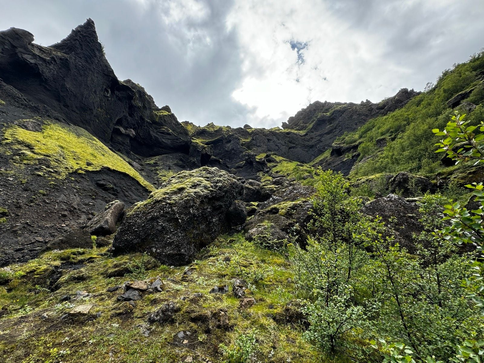 Moosbedeckte Felsen und dunkler Vulkangestein steigen unter einem bewölkten Himmel bei Tindfjöll an.