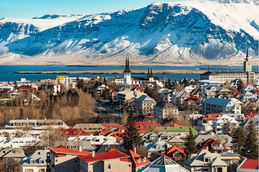 Reykjavik cityscape with colorful roofs, church spires, and snow-capped mountains across the bay.