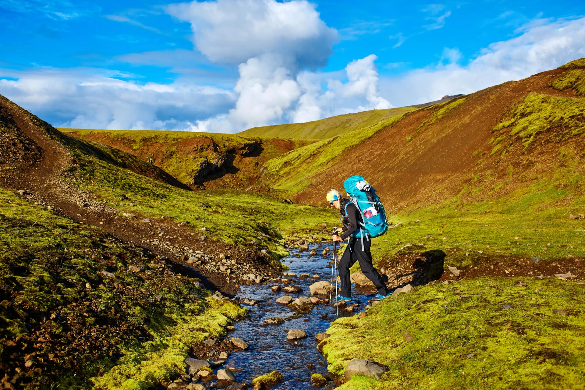 Viajar a Islandia. Hermoso paisaje islandés con un excursionista que atraviesa un arroyo, montañas, cielo y nubes. Senderismo en el parque nacional Landmannalaugar