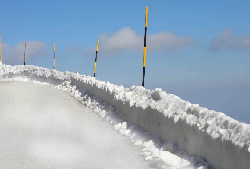 poles painted yellow and black stuck in the snow to delimit the edge of the icy mountain road