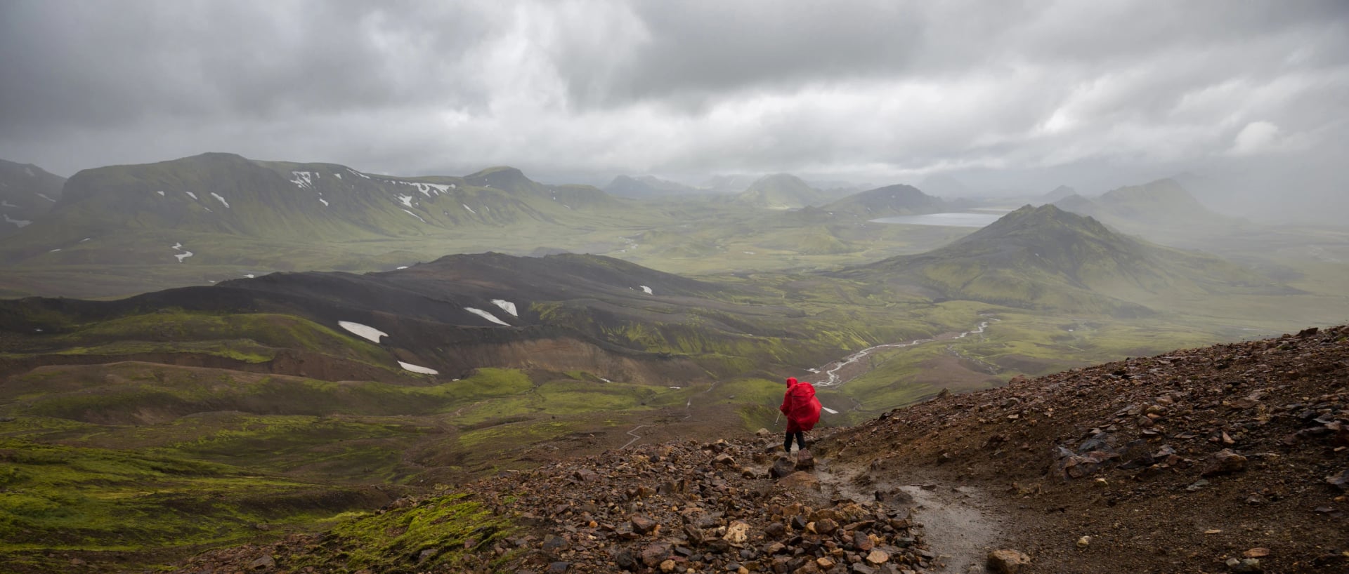 A person in a red rain cape hiking the Laugavegur trail in Iceland with a breathtaking view into a valley.