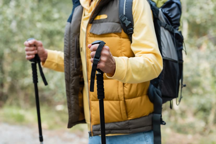 partial view of tourist wearing warm vest and standing with trekking poles outdoors