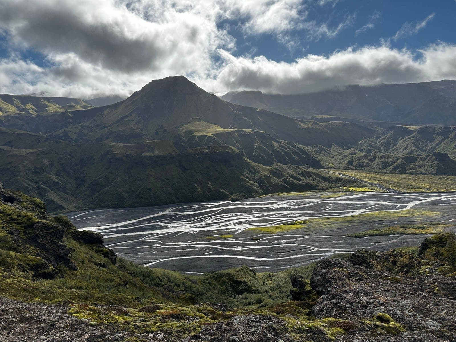 Volcanic landscape in Thorsmork with braided glacial river and green mountains under cloudy sky.