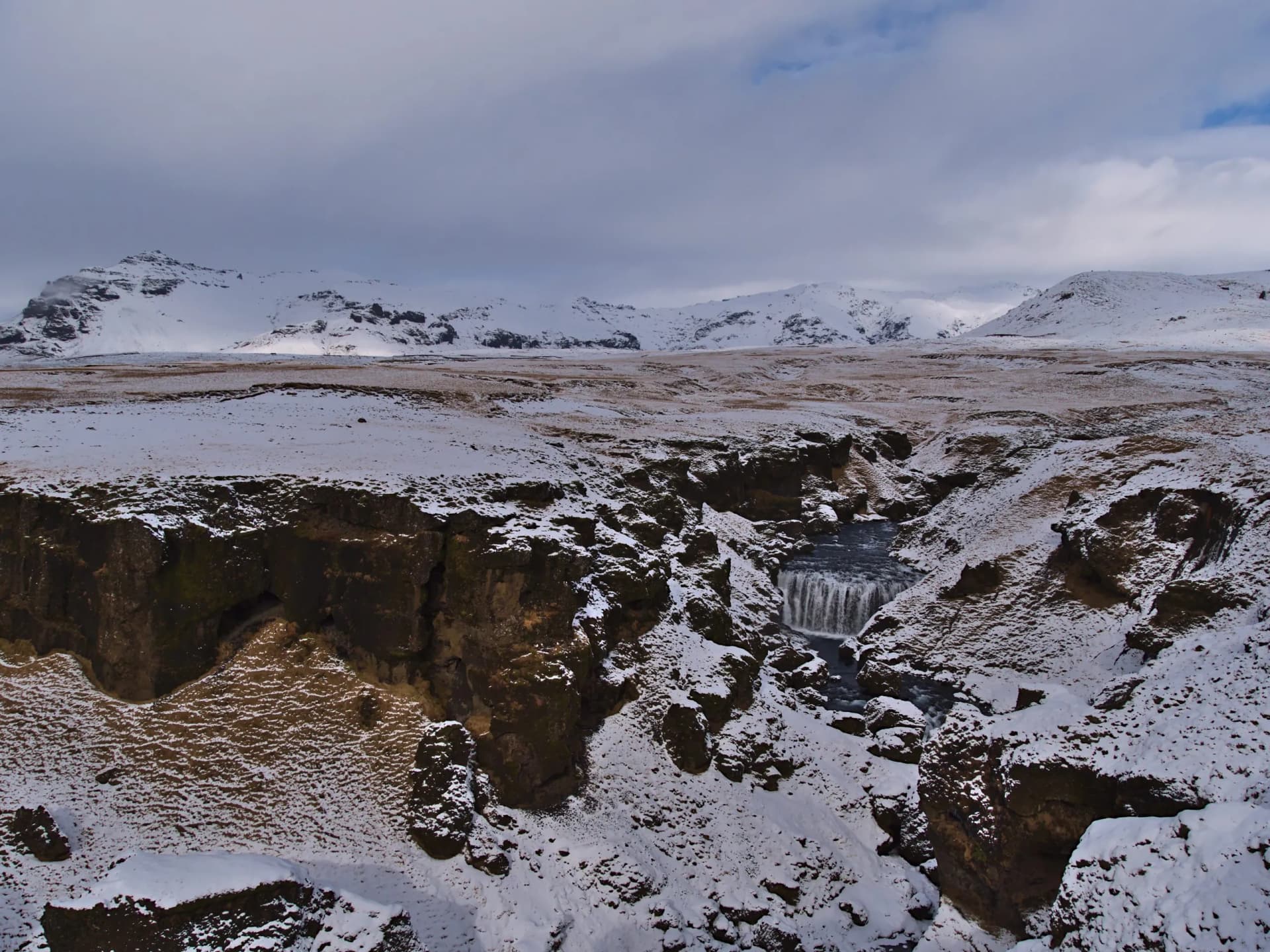 Beautiful view of Skógá river with waterfall Steinbogafoss in a rocky canyon near Fimmvörðuháls trail in winter with snow-covered meadows and rugged mountains in the south of Iceland.