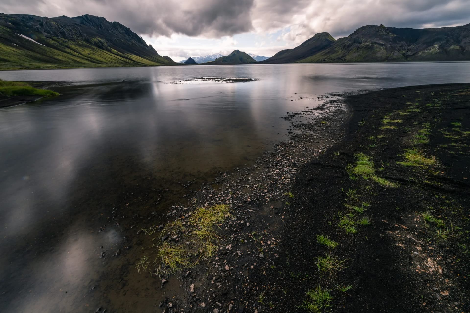 Lake Alftavatn in Iceland mountains with dark volcanic shore and cloudy sky reflections