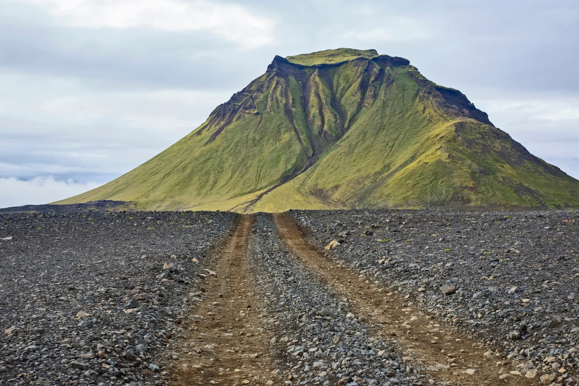 Mountain Hattfell in Iceland with green slopes above a rocky, barren foreground and dirt track.