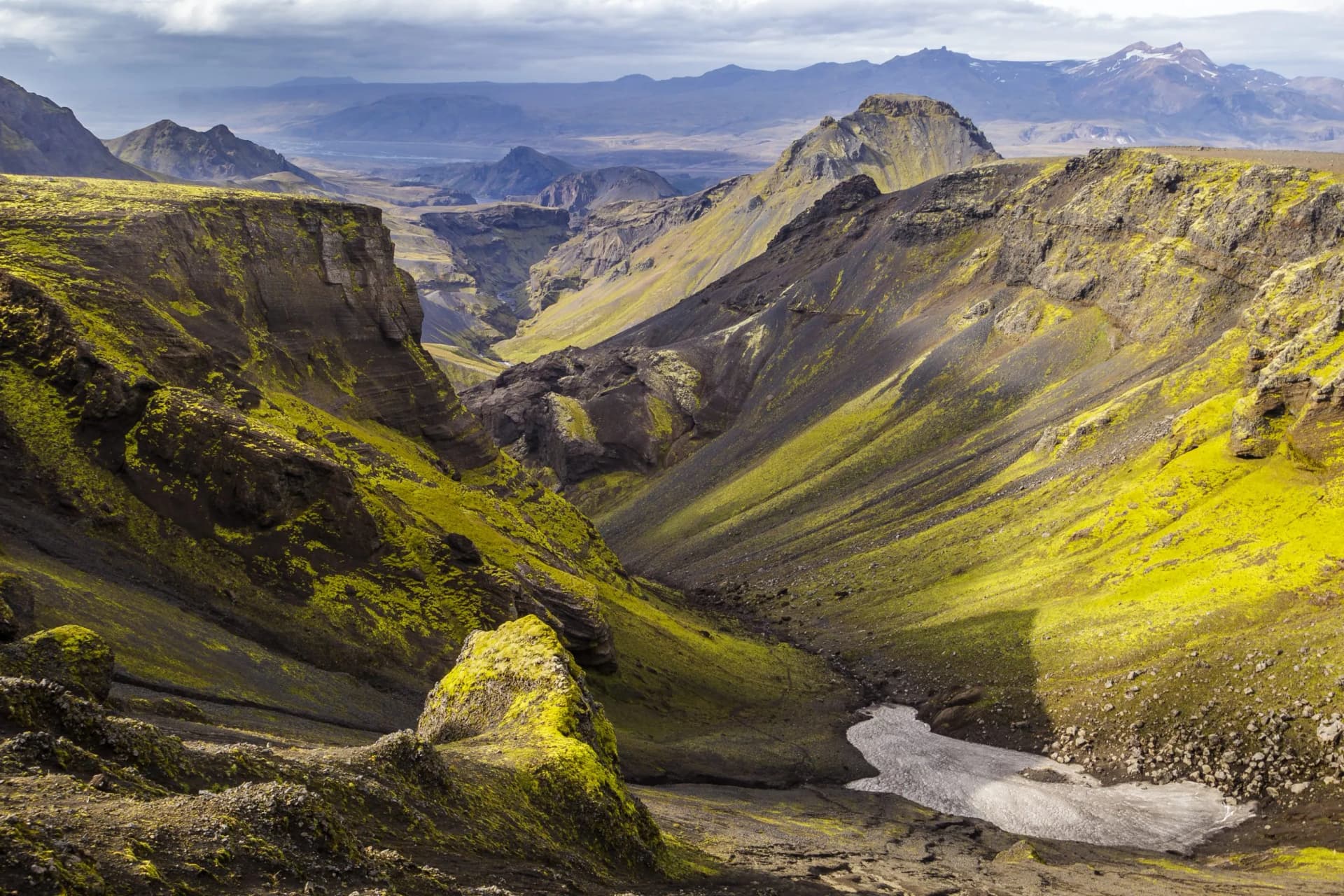 Hiking on Fimmvörðuháls in summer through a canyon with bright green moss and distant mountains.